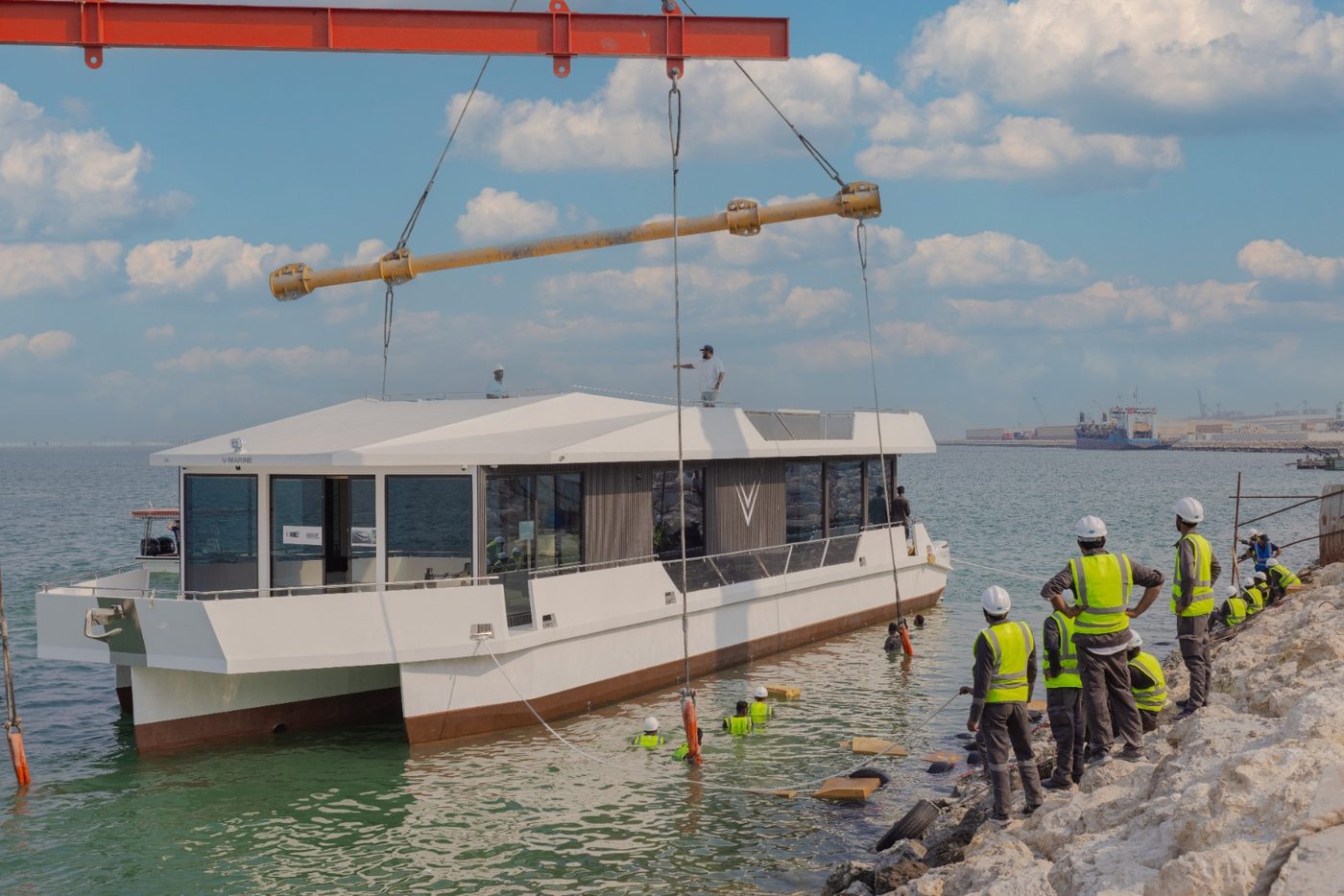 A completed V-Marine catamaran lowered into the sea by crane while the yard team looks on