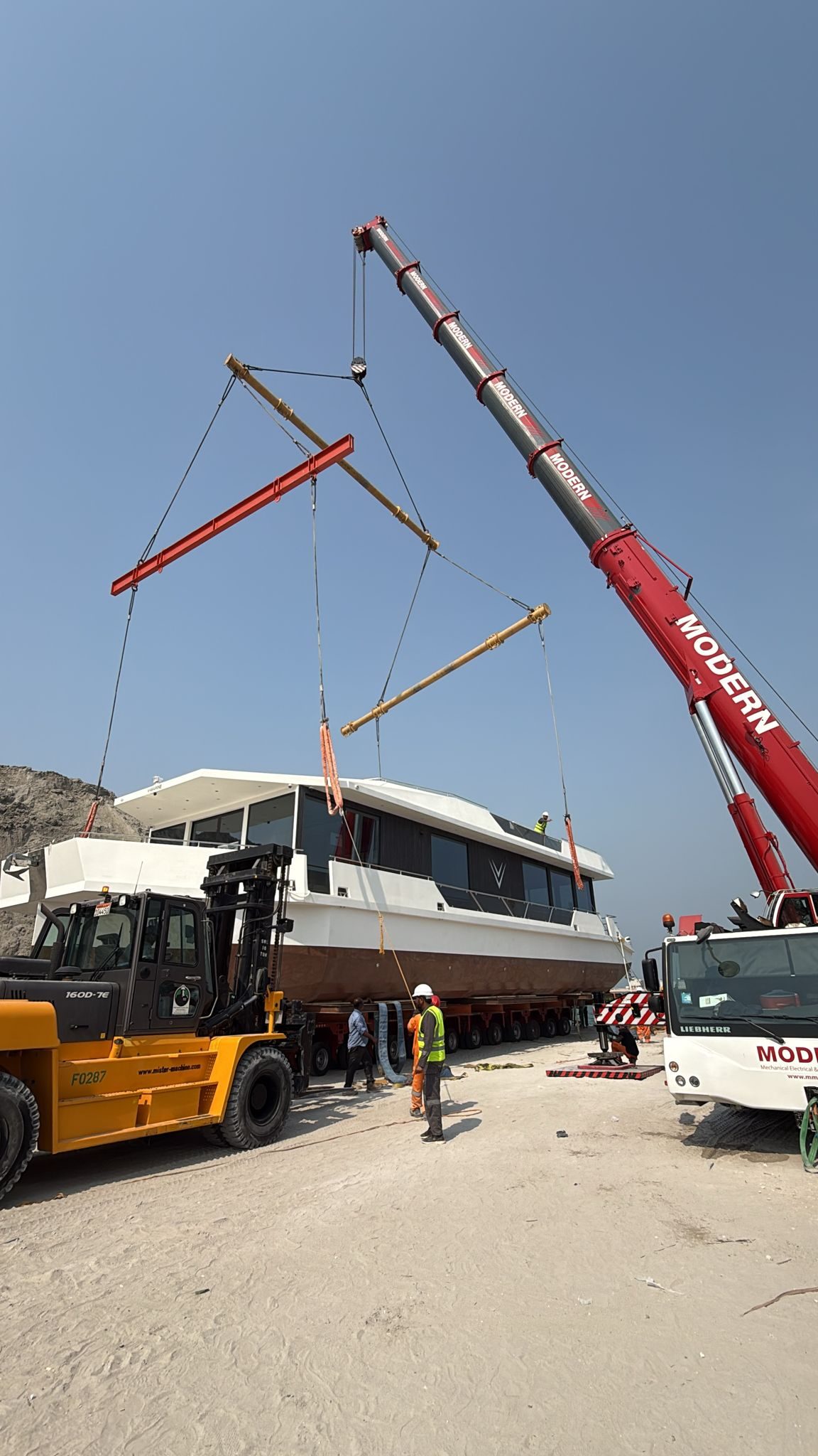 A finished V-Marine hull standing on multi-axle trailers with a mobile crane alongside